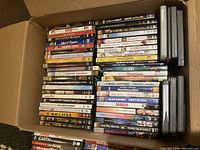 Open cardboard box packed with rows of DVD cases showing assorted movie titles
