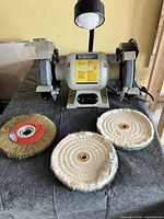 Front view of bench grinder showing lamp, eye shields, abrasive wheels, accessories on table