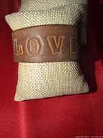Front view showing embossed “LOVE” lettering on brown leather cuff bracelet