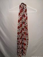 Full view of long ivory scarf with red cardinal and holly print on hanger