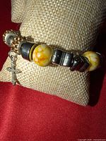 Bracelet on display pillow showing charms including cross, yellow beads, spacers