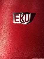 Front view of EKU enamel lapel pin on red background