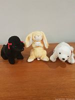 Black dog, yellow rabbit, white seal plush lined on wood surface