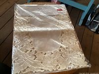 Sealed package showing folded cream floral lace table runner
