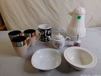 Group shot of all nine items: carafe, teapot, bell, two bowls, four mugs