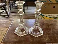 Full view of both matching clear glass candlesticks standing upright on wooden surface
