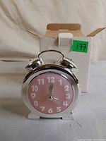 Front view of silver alarm clock style coin bank with pink face and box