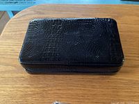 Closed case showing black faux alligator exterior and zip closure