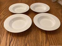 Four white rimmed soup bowls placed face up on wooden surface