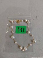 Full view of gold-tone chain necklace with faux pearls in plastic bag labeled 141