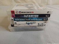 Stack of five PS3 game cases showing spines NFL Head Coach 09, Infamous, Karaoke Revolution: American Idol Encore, NHL 2K8 plus two additional cases underneath