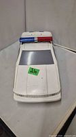 Front view showing white plastic police car toy, red/blue light bar, tinted windshield, wear marks