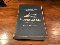Front cover of Royal Canadian Navy Signalman manual on wooden surface