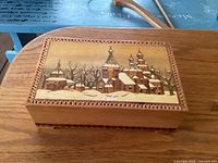 Lid showing painted winter village scene and carved border