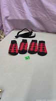 Four red and black plaid dog booties with black strap on table