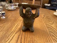 Front view of soapstone figure kneeling, arms raised supporting slab