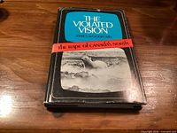 Front view of The Violated Vision book showing dust jacket and red wrap band