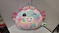 Front view of unicorn plush pillow showing embroidered face, horn, wings, tags
