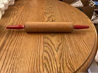 Rolling pin lying on wooden surface showing full body and red handles