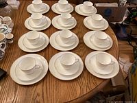Overview of 12 cup, saucer and plate settings arranged on table