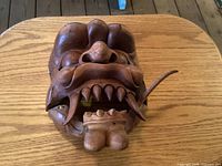 Front view of carved wooden demon mask showing overall design and one missing fang