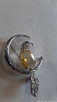 Brooch front view showing yellow crystal bird on silver crescent moon with rhinestones