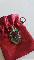 Front view of fruit pin on red pouch showing crystal body and enamel leaves