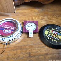 Three clocks laid on floor: Montreal Canadiens neon clock, square burgundy clock, NASCAR Nextel clock