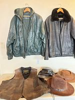 Two leather jackets on hangers, vest and two hats on table
