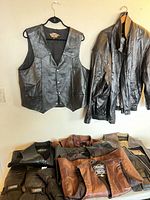 Overview of hanging Harley-Davidson vest, black leather jacket, five folded leather vests/jackets, two pairs gloves