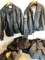 Two leather jackets on hangers and pile of additional jackets and hats