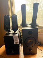 Logitech and Harman/Kardon speaker sets side by side showing satellites and subwoofers