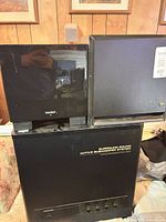 Front view of three black subwoofer cabinets, two cube-shaped stacked on a larger rectangular unit