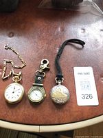 Three watches laid out: Westclox pocket watch, clip watch, ornate pocket watch