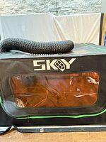 Front view of SKGY enclosure showing black fabric, green trim, clear window and vent hose on top