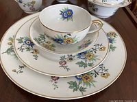 Close-up of stacked dinner plate, bread plate, saucer and teacup highlighting floral pattern and gold rim