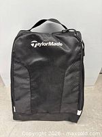 Front view of black TaylorMade shoe bag showing logo and mesh-textured panels
