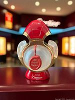 Front view showing red cap, gold trim, frosted panther heads, clear window with medallion, Cartier mark on base