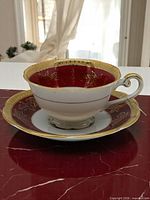 Tea cup on saucer showing red interior, gold filigree, gilded handle and rim