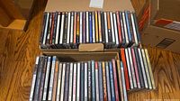 Two open boxes filled with rows of CD jewel cases (~80 total) on hardwood floor
