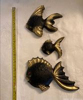 Front view of three chalkware fish with tape measure for scale