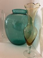 Teal bulbous vase behind amber fluted vase