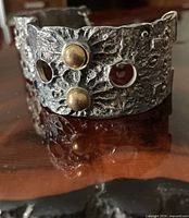 Front view of Robert Larin cuff showing textured pewter surface, brass studs, circular cutouts