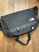 Front view of closed bag showing logo, flap and buckles