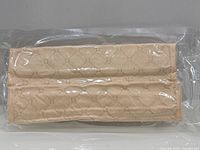 Front view of sealed package containing two beige quilted shoulder pads