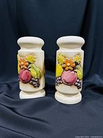 Front view of both ceramic shakers showing fruit relief decoration