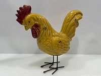 Front view of yellow ceramic rooster figurine showing red comb and metal legs