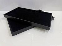 Top view of two black rectangular jewelry display trays, velvet interiors visible
