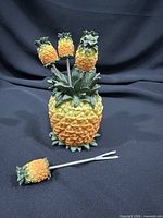 Pineapple holder with several picks inserted and one pick beside showing detail