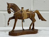 Full left side view of wooden horse figurine showing leather tack and oval base
